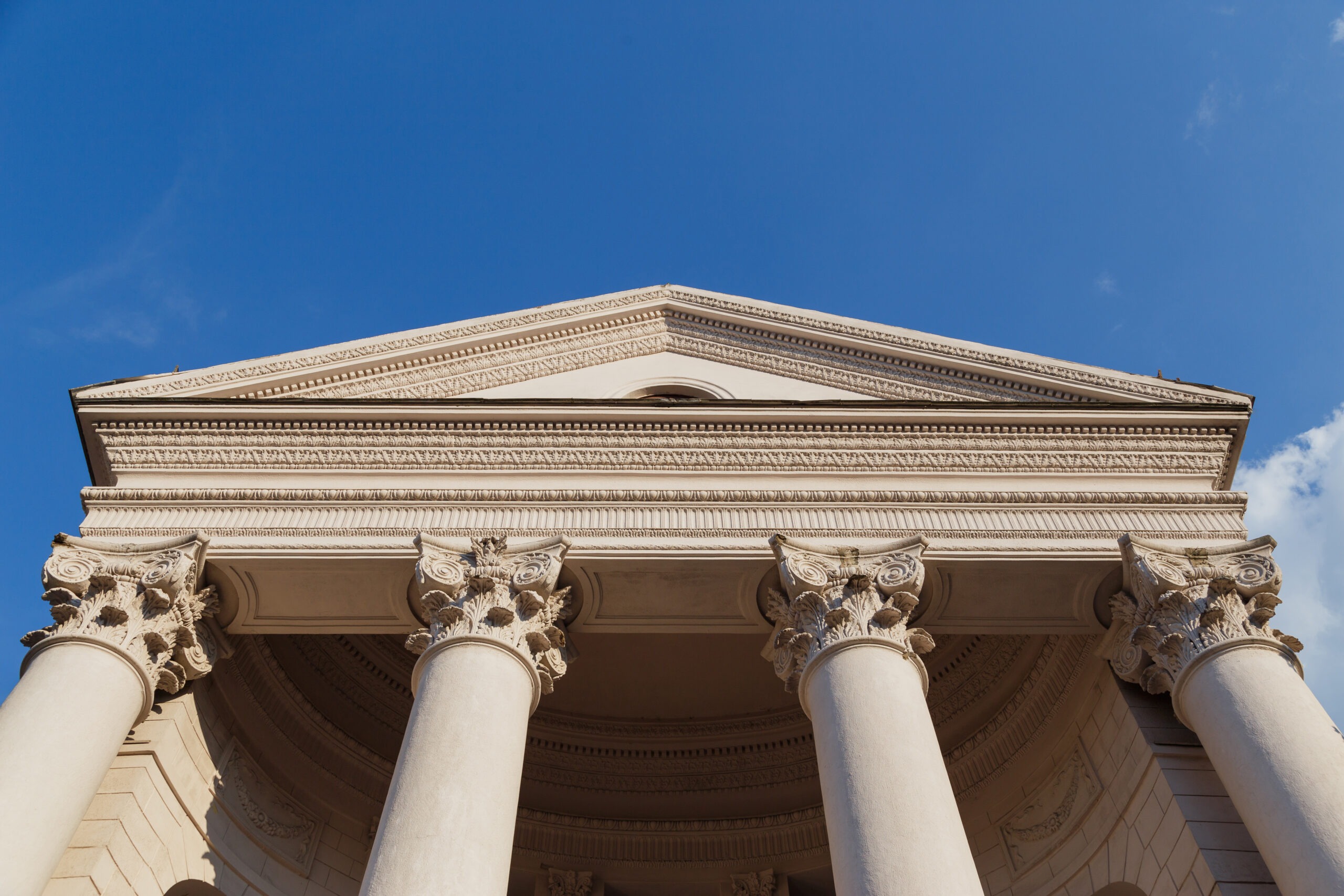 Capitol classical façade with columns beneath a blue sky background as seen from the bottom looking up.