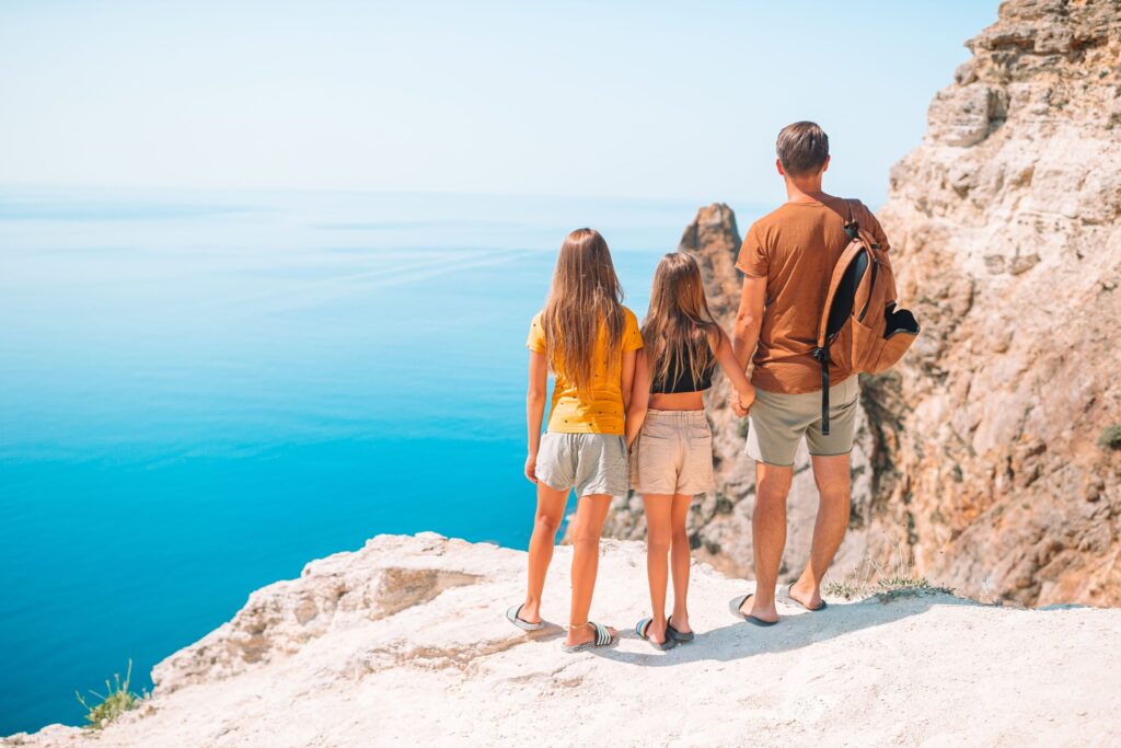 Father with kids on the beach standing atop a cliffside overlooking the ocean.