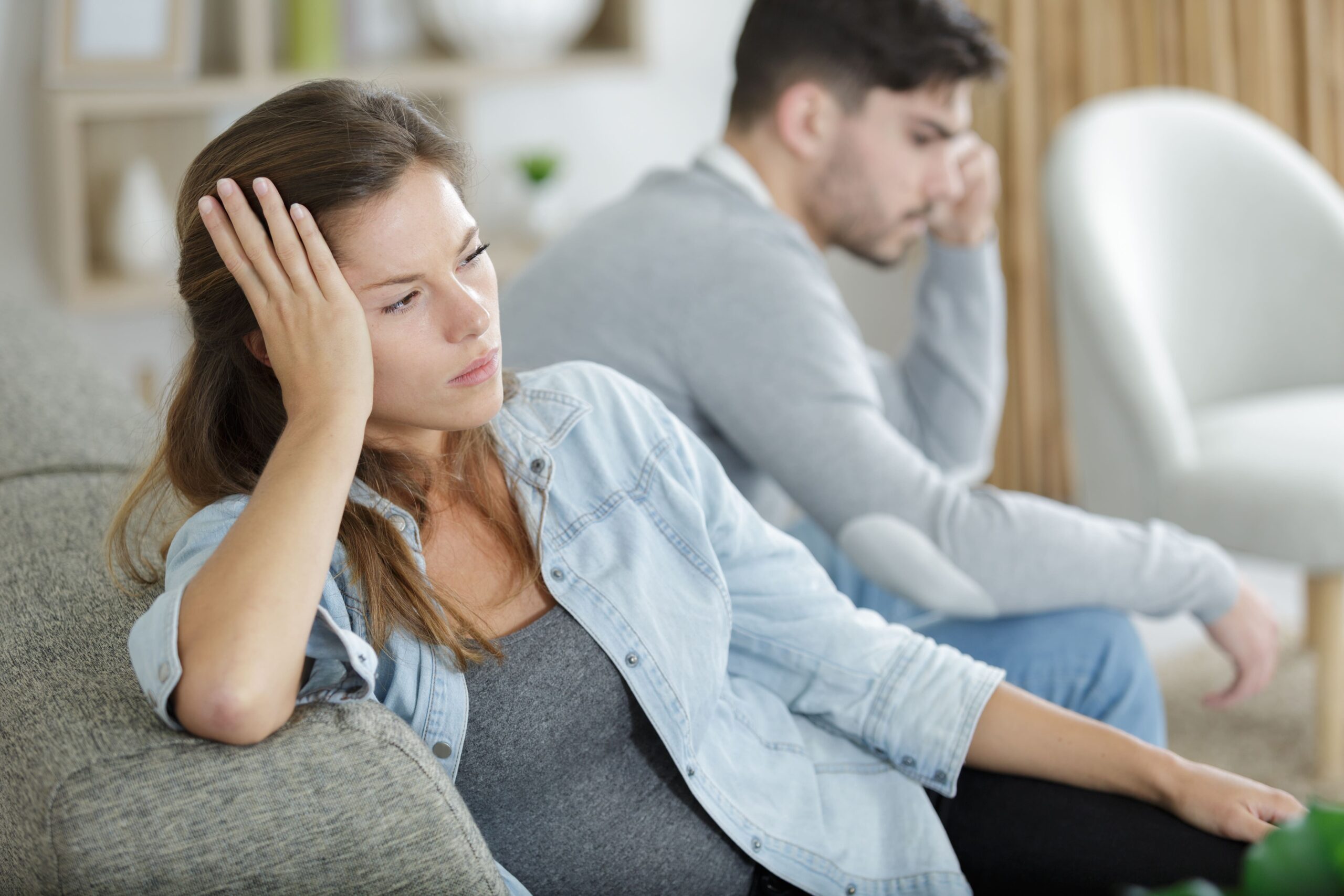 Woman sits on couch feeling distant from her husband.